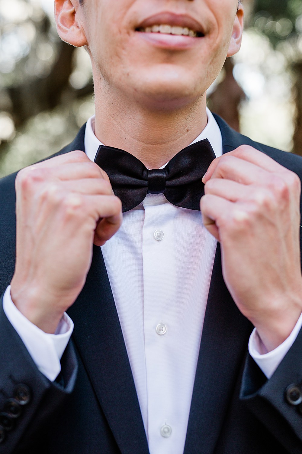 Groom smiles while adjusting his black bow-tie