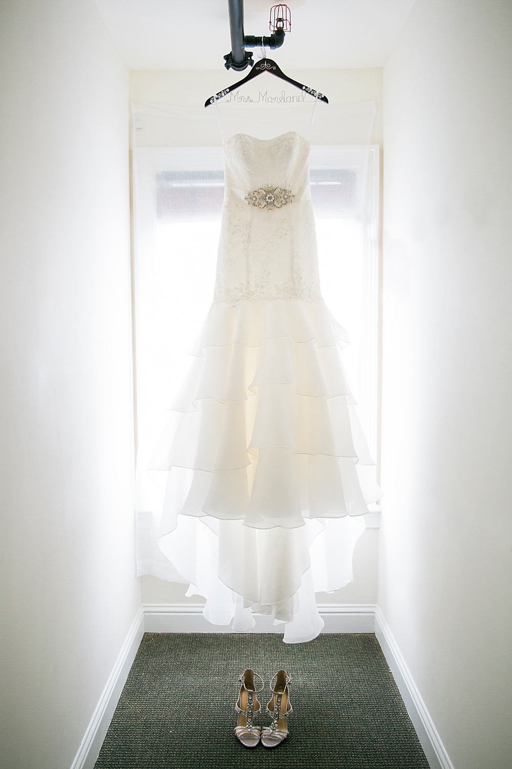 Bride's ruffled white dress and strappy heels hang in the attic of st. john's country club