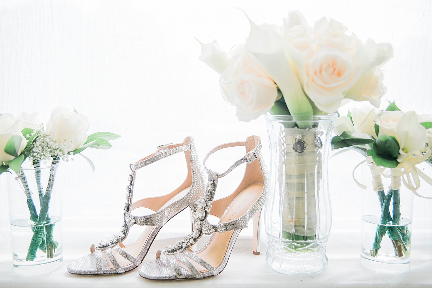 Silver heels and white rose bouquets sit on a window ledge