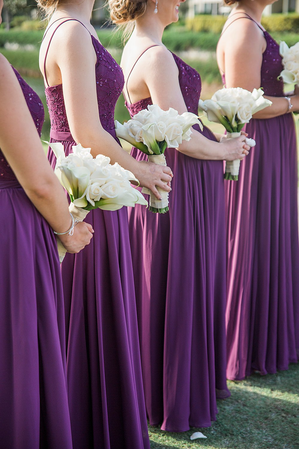 Bridesmaids in deep purple dresses holding white rose bouquets