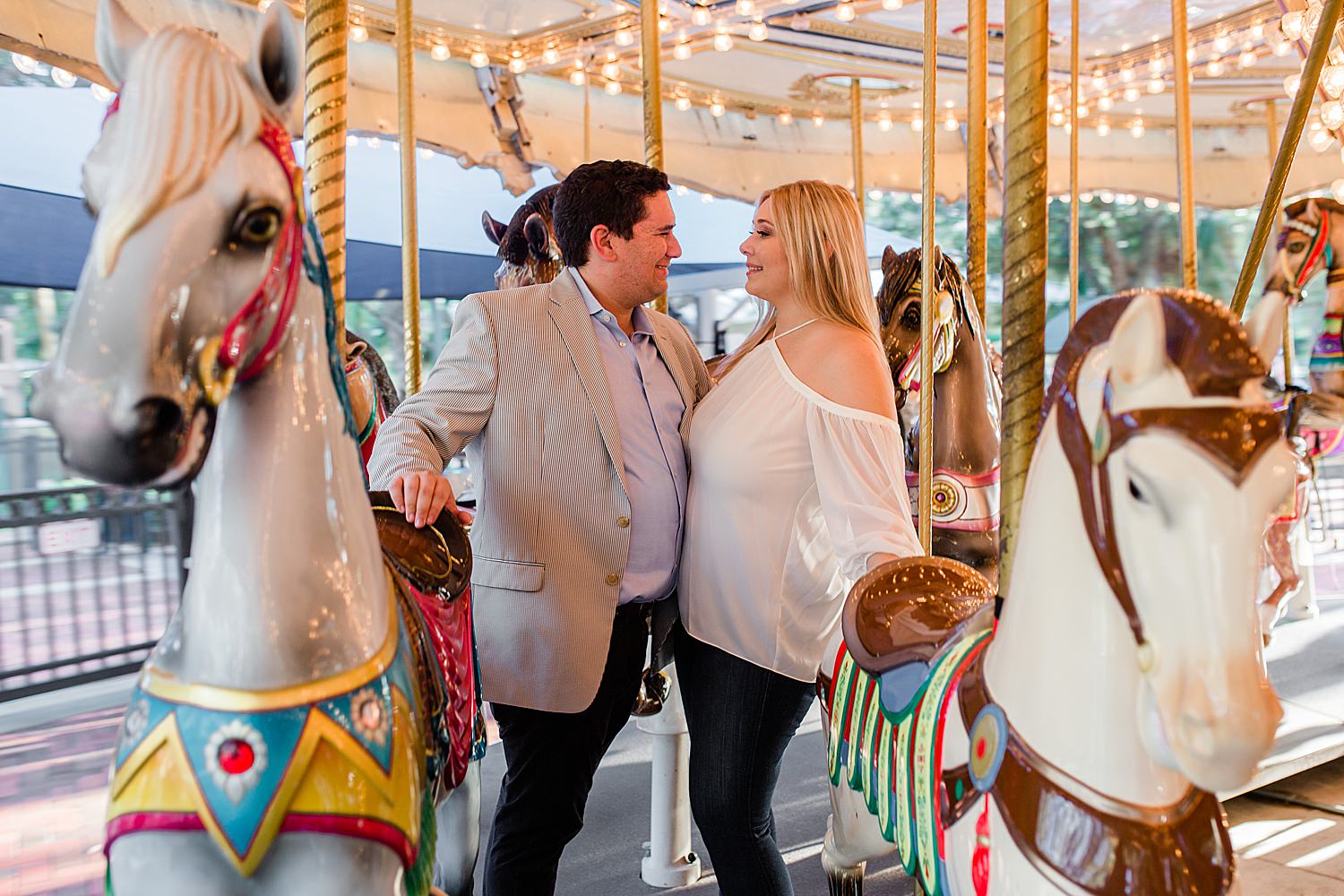 Couple smiles at each other in between horses on a carousel ride