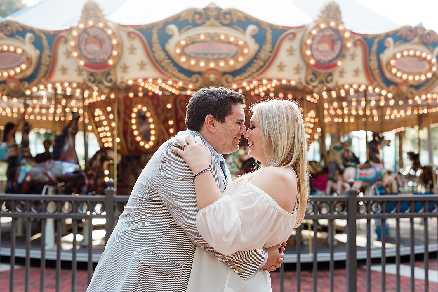 Couple shares eskimo kisses and smiles big in front of a carousel