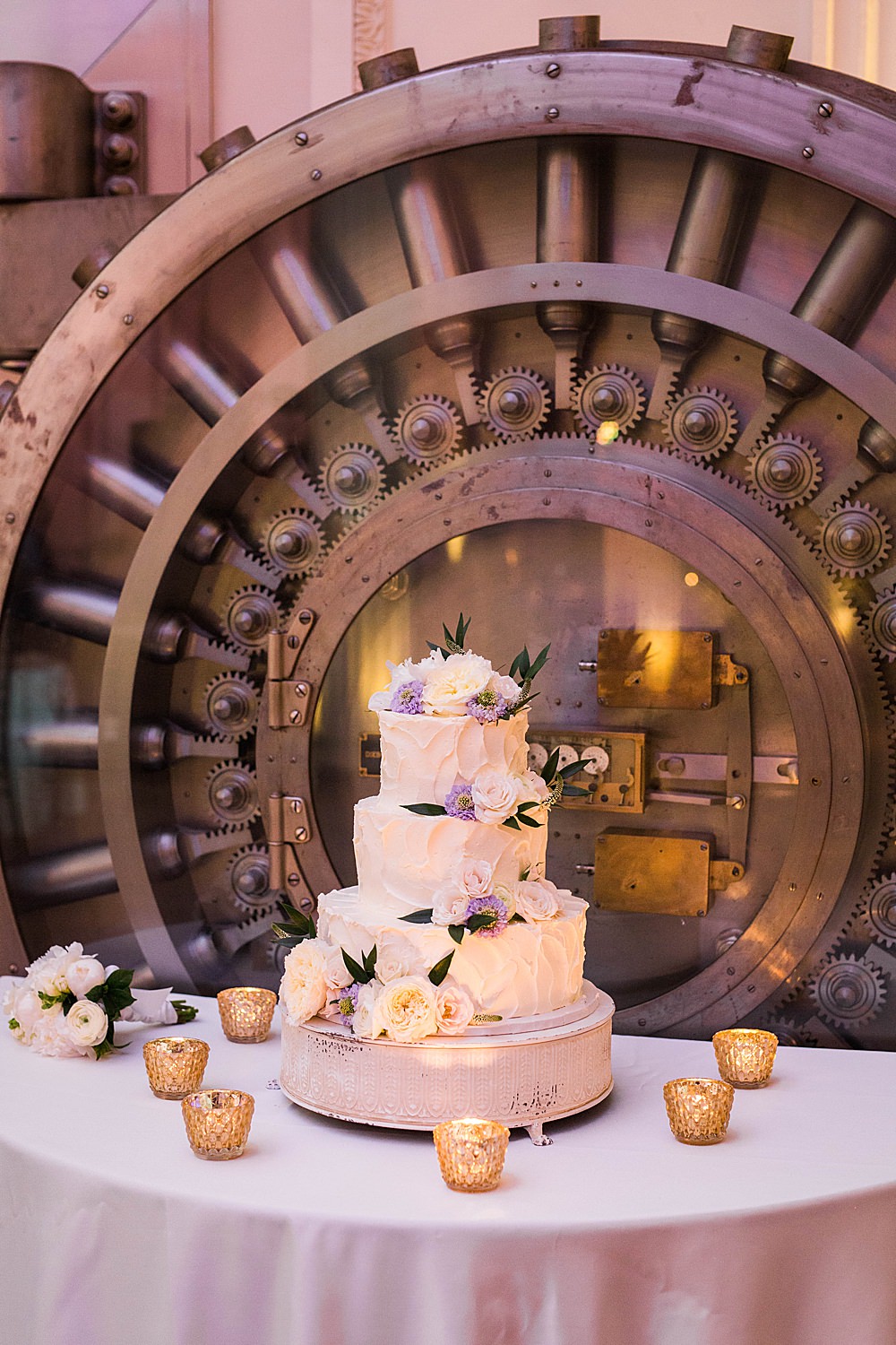Wedding cake sits on a candle lined table outside bank vault door at the treasury st augustine
