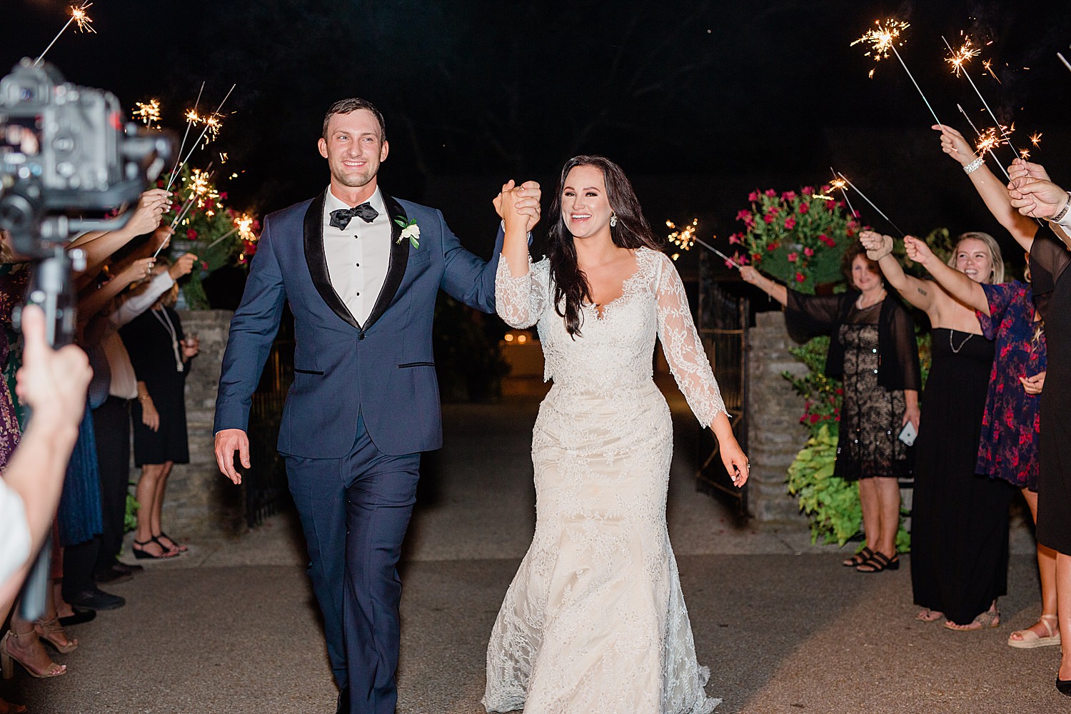 Bride and Groom smile holding hands as they exit their wedding surrounded by sparklers