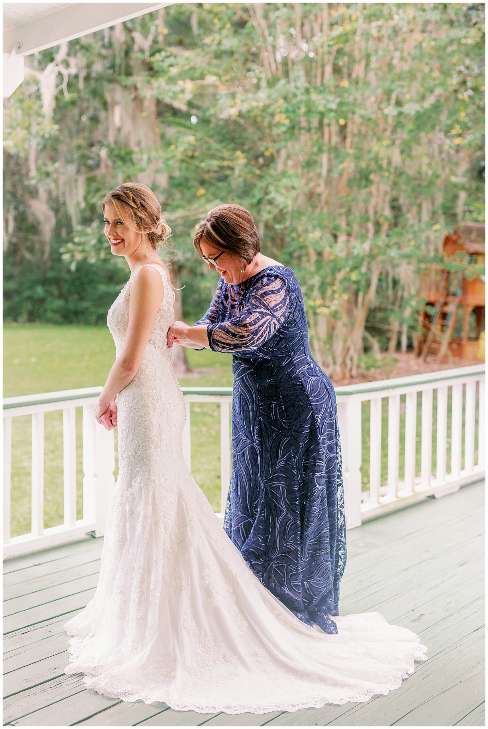 Bride's mom dressed in navy blue gown helps zip up her daughter's dress and she gets ready for her wedding