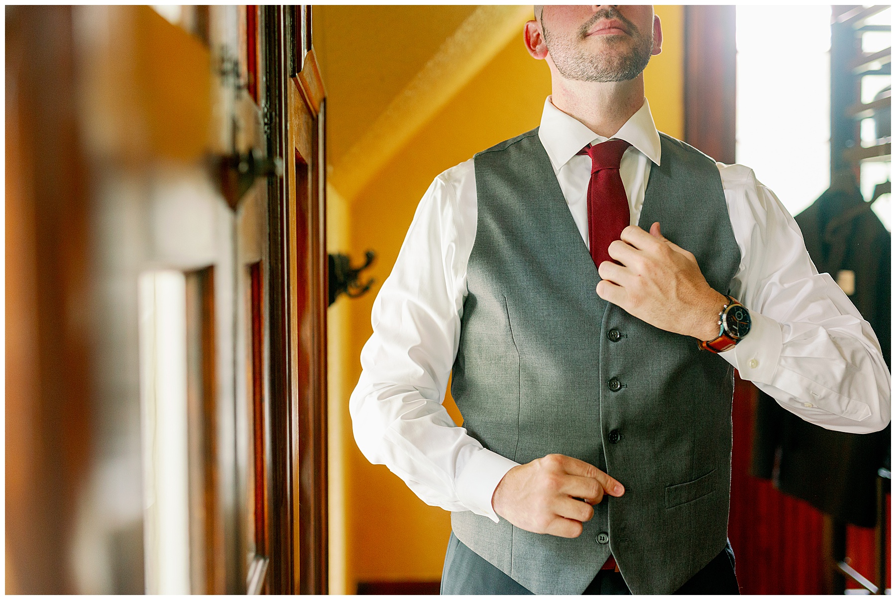 Groom gets ready for his wedding wearing a grey suit and burgundy tie